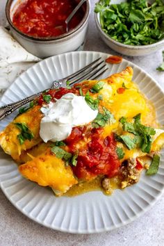 a white plate topped with an enchilada covered in sauce and sour cream