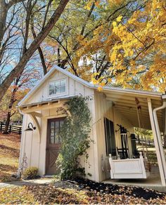 a small white house with porch and front door in the fall leaves, surrounded by trees