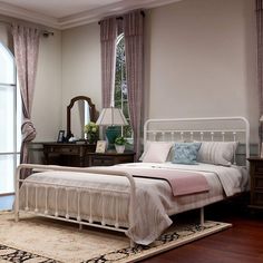 a white bed sitting on top of a wooden floor next to a dresser and mirror