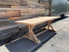 a wooden table sitting on the side of a road in front of a wall covered with wood planks