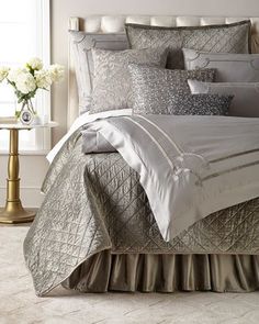 a bed with silver and white comforters in a room next to a window on the floor