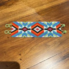 a colorful beaded bracelet laying on top of a wooden floor next to a pair of scissors