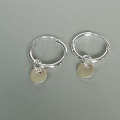 A PAIR of sterling silver hoops. Comes with a detachable tiny and delicate round disc charm. The charm is multipurpose and can be used with a neck or bracelet chain too. Dimension: Hoop- 12x1.2 mm Charm- 5 mm Drop length- 17 mm Price listed is for ONE PAIR These are made of 925 hypoallergenic sterling silver. Most of my pieces come with a 925 stamp. Can be packaged in a gift box. I can include a personal message from you if needed You are welcome to contact me at... bhavnakwintra1956@gmail.com F Silver Minimalist Huggie Dangle Earrings, Minimalist Silver Dangle Huggie Earrings, Minimalist Metal Round Huggie Earrings, Minimalist Round Metal Huggie Earrings, Nickel-free Minimalist Huggie Earrings, Everyday Round Charm Earrings, Minimalist Small Hoop Earrings With Charms, Everyday Round Earrings With Charms, Silver Huggie Earrings With Charms In Small Hoop Shape