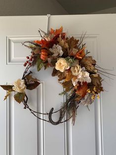 a wreath with flowers and leaves hanging on the front door to decorate it for fall