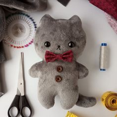 a teddy bear with a bow tie sitting next to scissors and thread