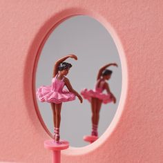 a toy ballerina is standing in front of a mirror with her reflection on the wall