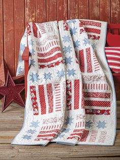 a red white and blue quilt sitting on top of a wooden bench next to a star