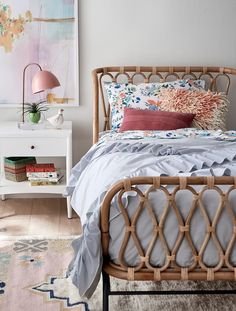 a wicker bed with pillows and blankets on it in front of a white dresser