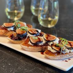 three slices of bread topped with figs and sauce on a plate next to wine glasses