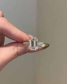 a woman's hand holding a ring with an emerald and diamond center stone on it