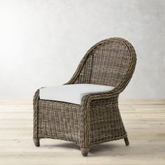 a wicker chair with white cushion sitting on a wooden floor next to a wall