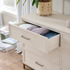 an open drawer in a white dresser next to a potted plant