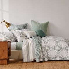 a bed with pillows and blankets on top of it next to a night stand in a room