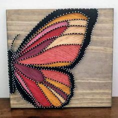 a colorful butterfly painted on top of a wooden block with beaded trimmings