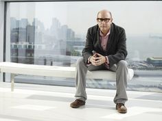 a man sitting on top of a white bench in front of a window next to a city