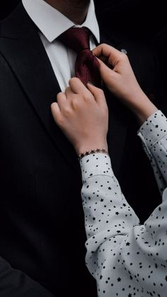 a man adjusting his tie while wearing a white shirt and black suit with stars on it