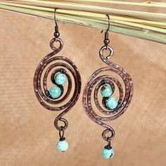 The classic elegance of the Armenian region merges with luminous jewels, bringing an exquisite design to life. Artisans Hasmik and Musheg work long hours with copper to create the spiral accents that compose these dangle earrings, whose antiqued finish is enhanced by reconstituted turquoise stones shining with ethereal and refreshing light. Unique Copper Wire Dangle Jewelry, Wire Jewelry Ideas, Gold Spiral Earrings Made Of Copper, Wire Wrapped Copper Spiral Earrings, Bohemian Spiral Copper Earrings, Bohemian Spiral Copper Wire Earrings, Hammered Wire Jewelry, Wire Earrings Handmade, Wire Jewelry Earrings