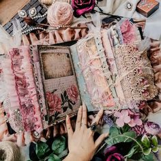 a person holding an open book on top of a table filled with flowers and other items