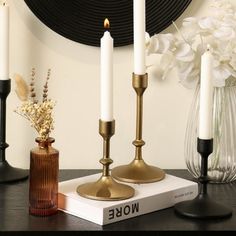 three candles are sitting on top of a book next to some vases and flowers