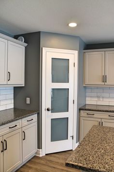 an empty kitchen with white cabinets and granite counter tops on the island in front of the door