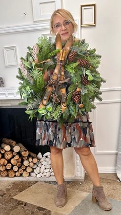 a woman standing in front of a fire place holding a wreath with pine cones and evergreens