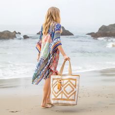 a woman is walking on the beach carrying a tote bag and looking at the ocean