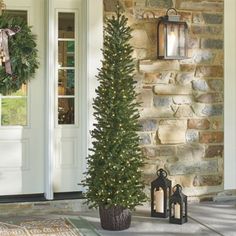 a christmas tree sitting on the front porch next to a lantern and lanterns with wreaths