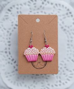 pink cupcake earrings with white sprinkles and hearts on them sitting on a card