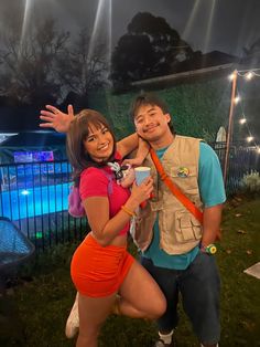 a man and woman posing for a photo in front of a swimming pool at night