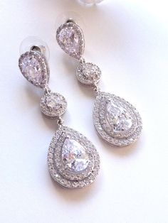 This earring features a white gold plated clear white teardrop cubic zirconia surrounded by 2 layers of little cubic zirconia gems (about 60 gems around it),  dangle from a white gold plated halo round cubic zirconia and a LARGE pear shaped cubic zirconia post earrings. Size: 5.3 (L) x 1.8  (W) cm or 2.1(L)  x 0.72  (W) inches long. Matching Bracelet and Necklace: https://www.etsy.com/listing/225770378/bridal-bracelet-double-halo-round-rose Note: The pear shaped post stud earring used in this design is sightly larger than my other design which has the similar post earrings. If it is a larger pear shaped post stud used, I will mentioned it as large in the listing and the title. **NOTE: CUBIC ZIRCONIA HAS MANY DIFFERENT GRADES, AND ALL THE CUBIC ZIRCONIA USED IN MY DESIGN IS OF THE HIGHEST Q White Diamond-accented Teardrop Earrings, White Diamond Accented Pear-shaped Teardrop Earrings, White Pear-shaped Teardrop Earrings With Diamond Accents, White Cubic Zirconia Teardrop Earrings For Party, Cubic Zirconia Drop Crystal Earrings For Anniversary, White Crystal Teardrop Earrings With Sparkling Detail, White Crystal Teardrop Earrings With Sparkle, White Sparkling Crystal Teardrop Earrings, Drop Crystal Earrings With Cubic Zirconia For Anniversary