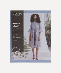 an advertisement for liberty fabrics featuring a woman in a floral dress and brown shoes, with palm trees behind her