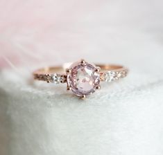 a pink diamond ring sitting on top of a white cloth with diamonds around it's edges