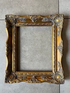 an ornate gold frame sitting on the floor in front of a tile wall with a gray background