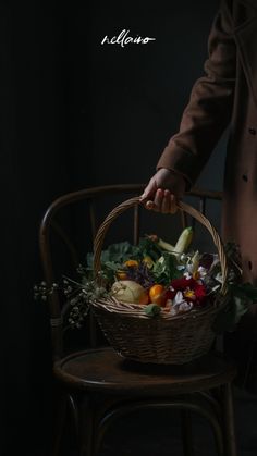 a person holding a basket with vegetables in it on top of a wooden chair next to a wall