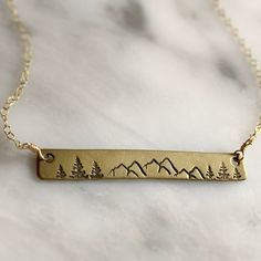 This brass bar necklace is a beautiful and unique piece of jewelry that captures the rugged beauty of the outdoors. Handmade in Colorado, the necklace features a 14k gold fill chain adding beauty and durability that will last. The brass bar pendant is stamped with a stunning design of mountains and pine trees. This necklace is perfect for anyone who loves the outdoors and wants to carry a piece of the mountains with them wherever they go. ● Solid Brass bar ● 14k Gold Fill 16” Chain ● Made by han Mountain Bar, Mountain Jewelry, Brass Bar, Outdoor Enthusiast, Bar Pendant, Pine Trees, Jewelry Inspo, Gold Filled Chain, Bar Necklace