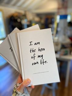 a person holding up three books with writing on the pages that read i am the hero of my own life