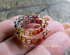 a hand holding two rings with different colored stones on it's sides and the middle one in yellow gold