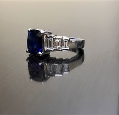 DeKara Designs Classic Metal- 90% Platinum, 10% Iridium. Stones- 1 Cushion Cut Ceylon Blue Sapphire 2.92 Carats. 6 Square Baguette Diamonds, F-G Color VS1 Clarity, 0.94 Carats. A beautiful dark blue Cushion Cut 2.92 Carat Ceylon blue sapphire and diamond platinum ring that is inspired by the Roaring 20's. The ring is true to its Art Deco look with the 3 accenting rectangle baguettes that are channel set with g color and vs1 in clarity totaling to .94 carats. The sapphire is set with four prongs Modern Sapphire Rings Gia Certified, Gia Certified Baguette Cut Sapphire Ring, Blue Diamond Platinum Ring With Polished Finish, Wedding Sapphire Baguette Cut Ring With Polished Finish, Blue Platinum Diamond Ring With Polished Finish, Polished Baguette Cut Sapphire Ring For Anniversary, Wedding Baguette Cut Sapphire Ring With Polished Finish, Sapphire Baguette Cut Ring For Anniversary, Baguette Cut Sapphire Ring With Polished Finish For Wedding