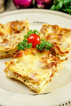 two slices of lasagna on a plate with parsley and cherry tomatoes in the background