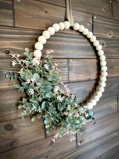 a white beaded wreath hanging on a wooden wall with greenery in the middle