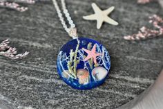 Bring a piece of the ocean with you wherever you go with our Pressed Flower "Under the Ocean" Pendant. This unique and eye-catching pendant features real blue lichen, starfish, sand, sea shells and abalone shells encased in eco-friendly resin colored with transparent inks to give it a sparkling water effect.The pendant comes with a  -1.5mm chain, 18" long, but if you prefer a different length, you can type it in the personalization box.  The pendant is available with  -925 sterling silver or  -s Ocean-inspired Jewelry With Starfish Charm As Gift, Ocean-inspired Jewelry With Starfish Charm For Gift, Adjustable Blue Necklace With Starfish Charm, Turquoise Starfish Ocean-inspired Jewelry, Ocean-inspired Adjustable Charm Necklace Gift, Ocean-inspired Sterling Silver Beach Jewelry, Ocean-inspired Blue Strand Jewelry, Blue Ocean-inspired Jewelry For Vacation, Blue Ocean-inspired Strand Jewelry