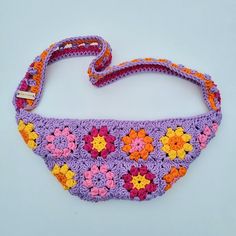 a purple crocheted purse with colorful flowers on it's side and a white background