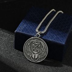 a silver necklace with an image of the egyptian god on it sitting next to a blue box