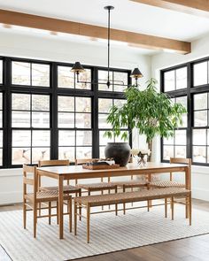 a dining room table with chairs and a bench in front of large windows that have black panes on them