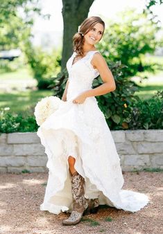 a woman in a white dress and cowboy boots posing for the camera with her bouquet