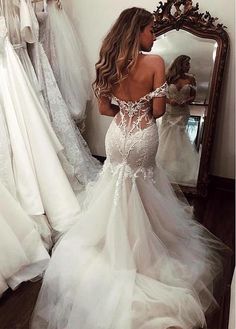 a woman standing in front of a mirror wearing a wedding dress with sheer sleeves and open back