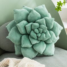 a green flower pillow sitting on top of a gray couch next to a white glove