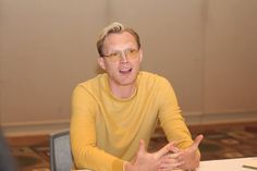 a man sitting at a table with his hands out in front of him and talking to someone else