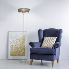 a blue chair next to a gold and white painting on the wall with a lamp