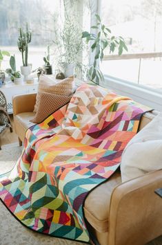 a living room filled with furniture and a colorful blanket on top of a couch next to a window